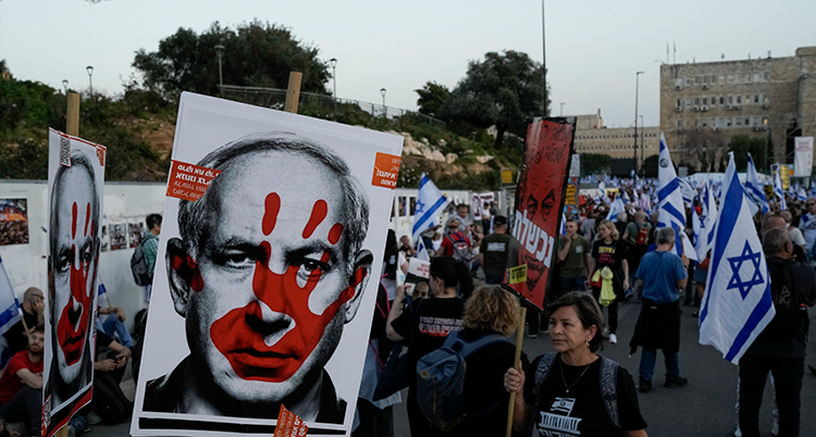 Folk har affischer med Netanyahus ansikte. En röd hand täcker hans ansikte.