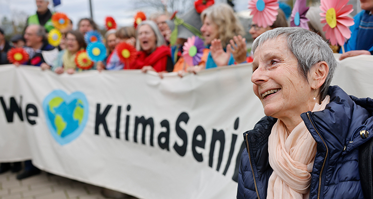 En kvinna ser glad ut. Hon står framför flera andra kvinnor som håller en banderoll.