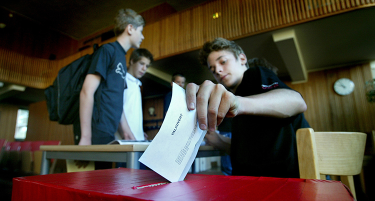 En ung kille lägger kuvertet i valurnan. Bakom syns två unga personer.