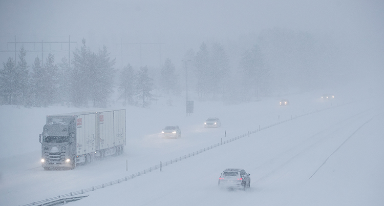 Några bilar kör på en motorväg. Det snöar mycket.