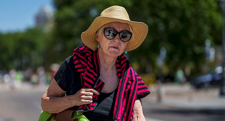 En kvinna är utomhus i solen i staden Madrid. Hon har på sig en hatt och solglasögon.