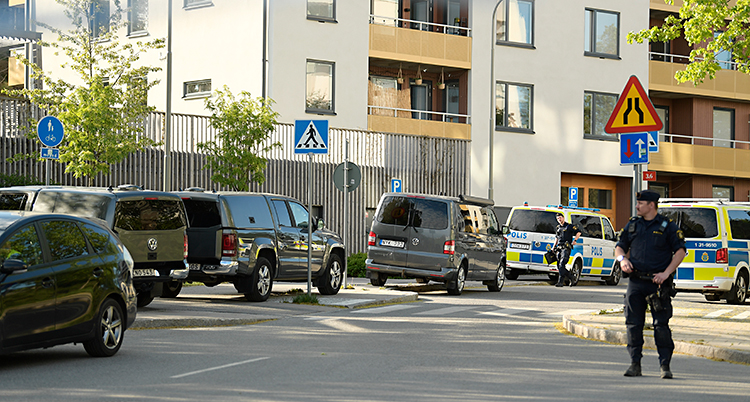Flera bilar och poliser står på en gata utanför ett hus med lägenheter.