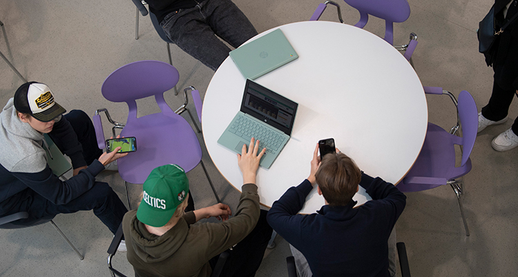 En bild tagen ovanifrån på elever som sitter vid ett runt bord med sina datorer.