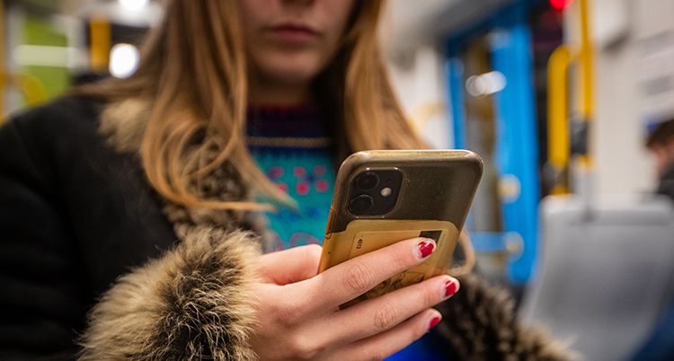 En ung kvinna sitter i en tunnelbanevagn och läser i mobilen.