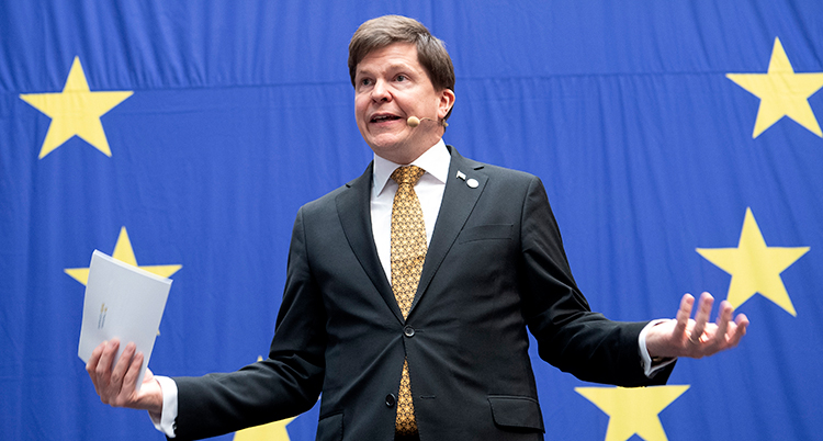 Han slår ut med armarna, han står framför en stor EU-symbol med stjärnor.