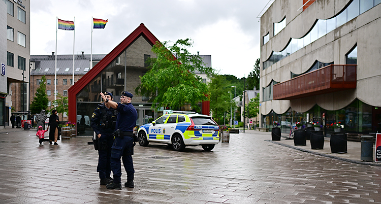 Två poliser står på ett torg och pratar. Bakom dem står en polisbil.