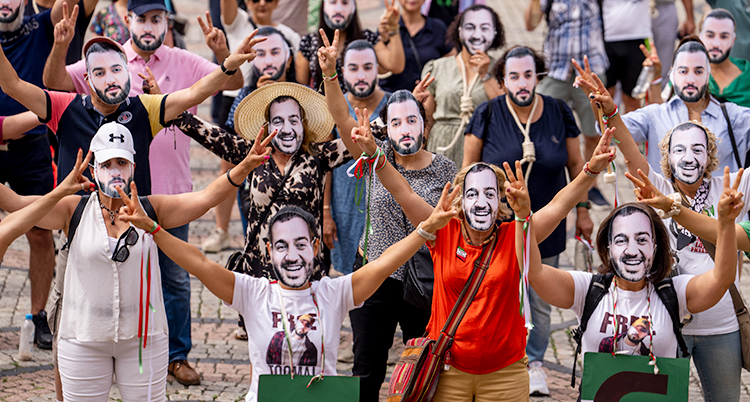 Flera personer går på gatan. De har masker för ansiktet som visar Toomaj Salehi.