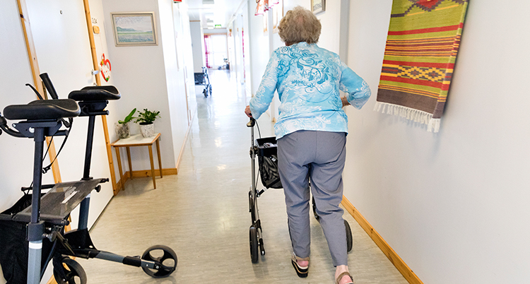 En äldre kvinna går med en rullator i en korridor.