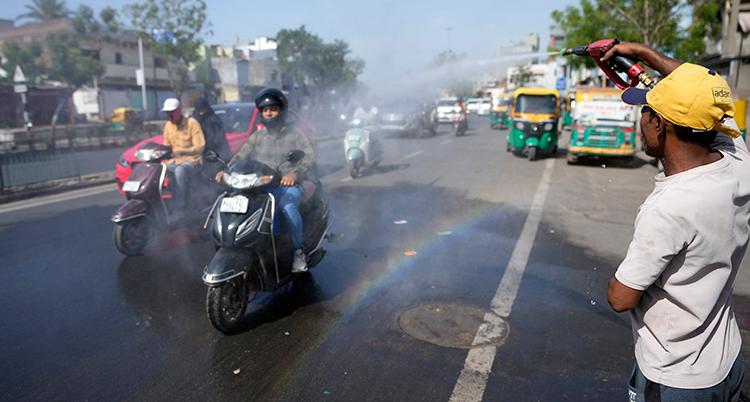 En man sprutar vatten på några trafikanter på mopeder.