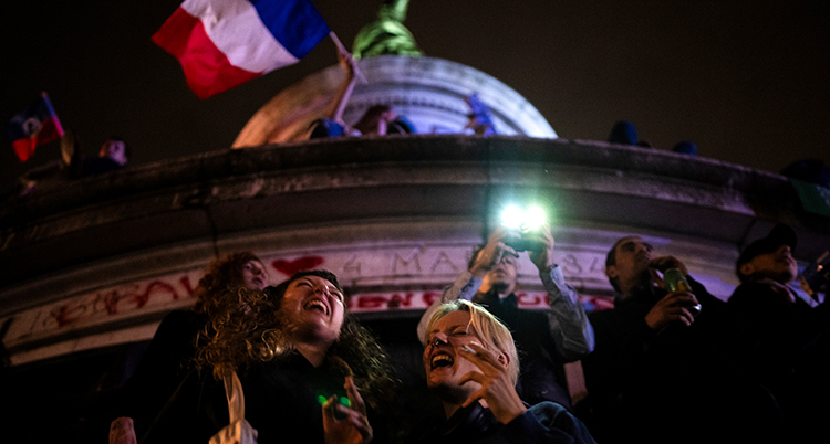 Glada människor i mörkret framför en stor byggnad med en fransk flagga.