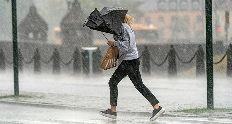 En kvinna går genom regn med ett trasigt paraply.