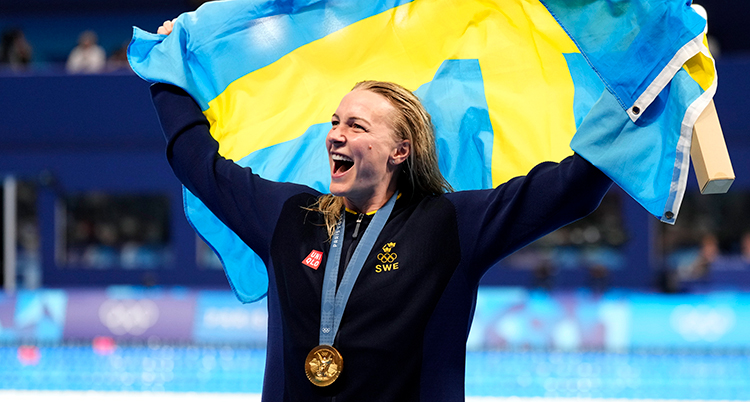 Sjöström jublar. Hon har medaljen runt halsen och håller upp en flagga.