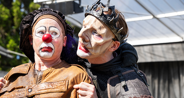 En person sminkad till clown står framför en person klädd till kung med en krona på huvudet.