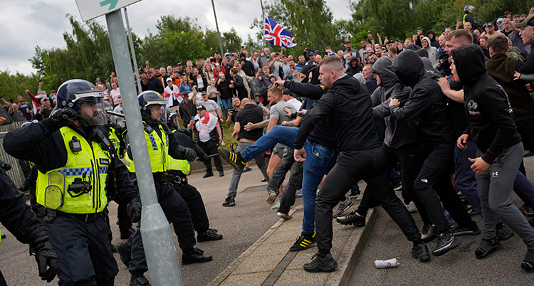 Många personer är på gatan. Flera av dem sparkar och slår mot poliser.