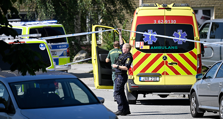 Flera polisbilar och en ambulans står på gatan. En polis står och håller upp ett avspärrningsband.