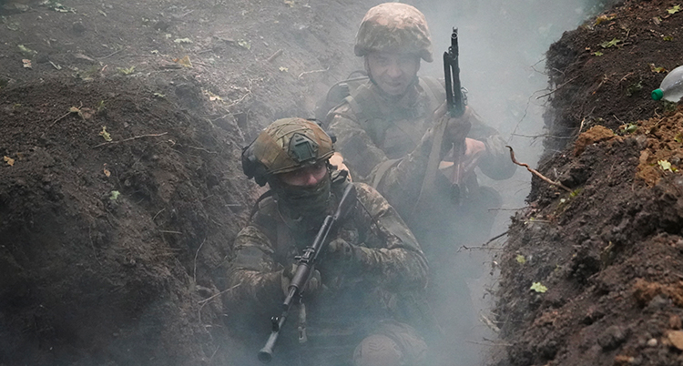 De sitter i ett dike. De har gröna militärkläder, hjälmar och vapen.