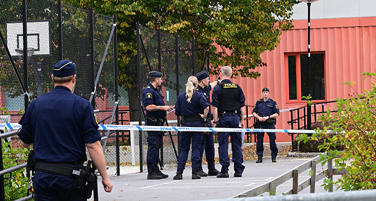 Flera poliser står bakom blå band utanför en skola med röd vägg.