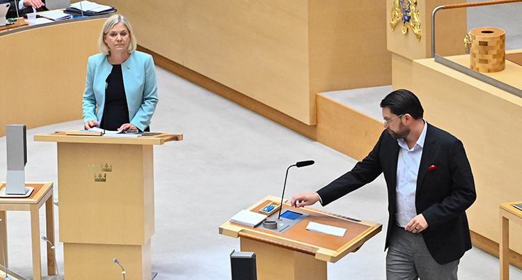 Magdalena Andersson står i en talarstol i riksdagen. Jimmie Åkesson står också i en talarstol.