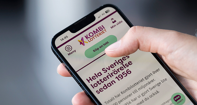 En hand som håller i en mobil. På mobilen är det Kombilotteriets sajt på internet.
