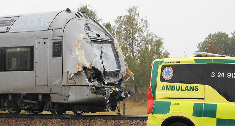 Ett tåg står stilla på rälsen. Framsidan på tåget är alldeles trasig. En ambulans står bredvid.