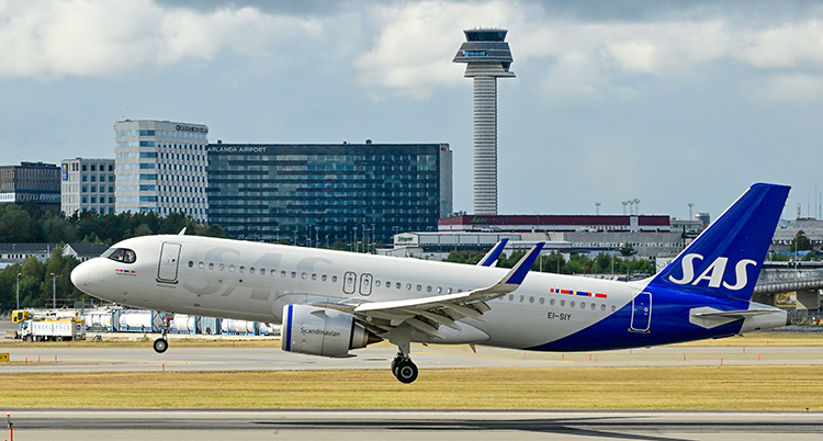 Ett flygplan från SAS lyfter på en bana framför byggnader.