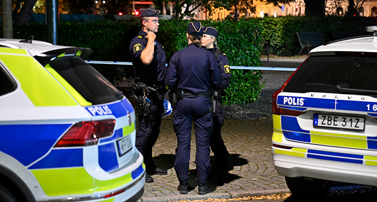 Poliser som står vid polisbilar och en polisavspärrning.