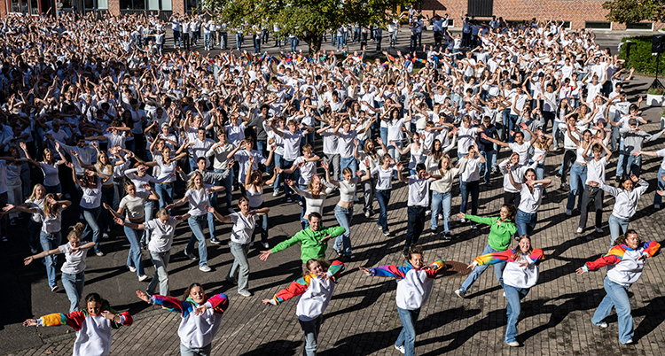 Många unga står på en skolgård. De dansar.