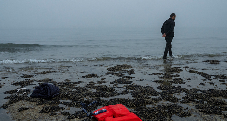 En person och en flytväst på en strand vid ett hav.