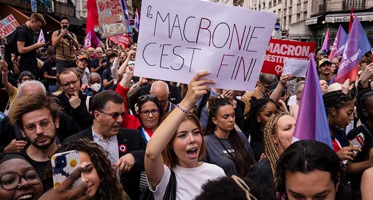 Många människor går på gatan. De håller i skyltar som protesterar mot ledaren Macron.