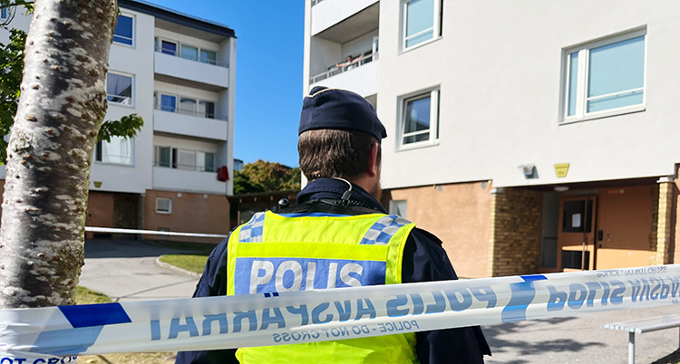 En polis står framför hus med lägenheter.