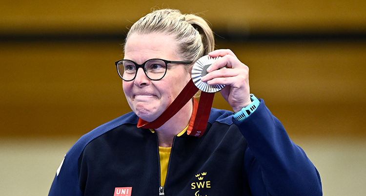 Hon är glad och håller upp en medalj som hänger runt halsen.