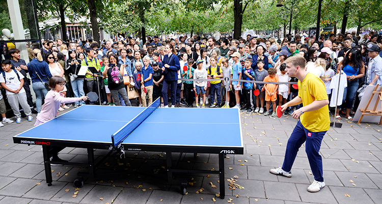 De spelar bordtennis. Bordet står i Kungsträdgården i Stockholm. Många tittar på när de spelar.