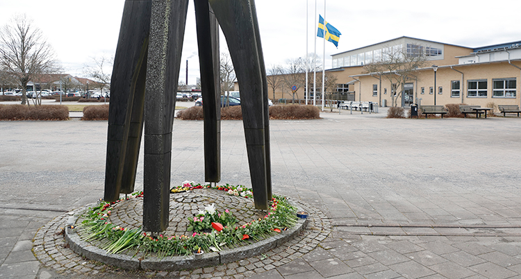 Människor har lagt blommor vid en skulptur. Skulpturen står utanför en skola.