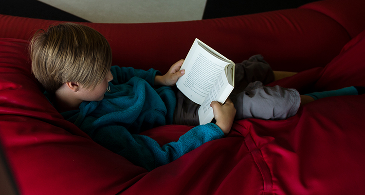 En pojke ligger i en soffa och läser en bok.