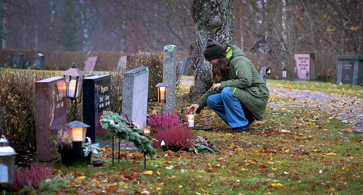 Kvinna tänder ett ljus vid grav på kyrkogård.