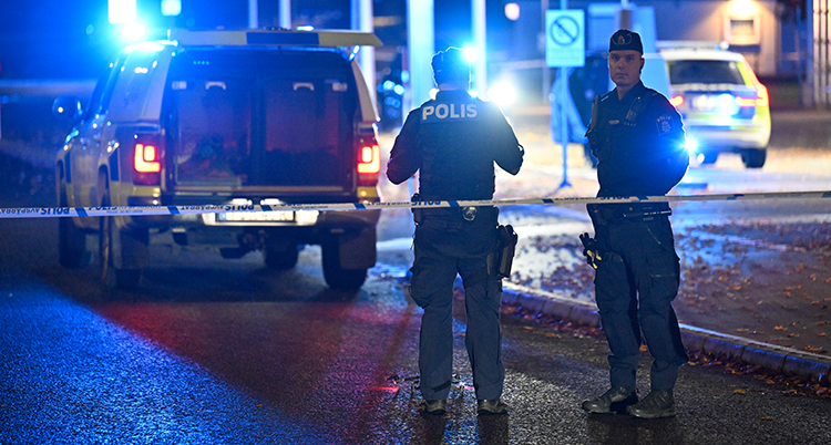 Poliser och polisbilar är utomhus i mörker. Det finns polisband.