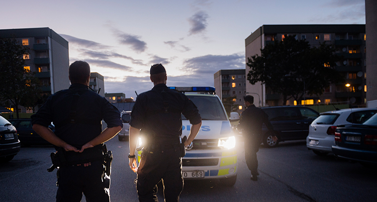 Det är kväll. Poliserna går på en gata. En polisbuss syns också.