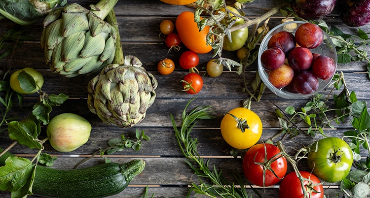 Flera grönsaker och frukt ligger på ett bord, till exempel tomat, äpple och squash.