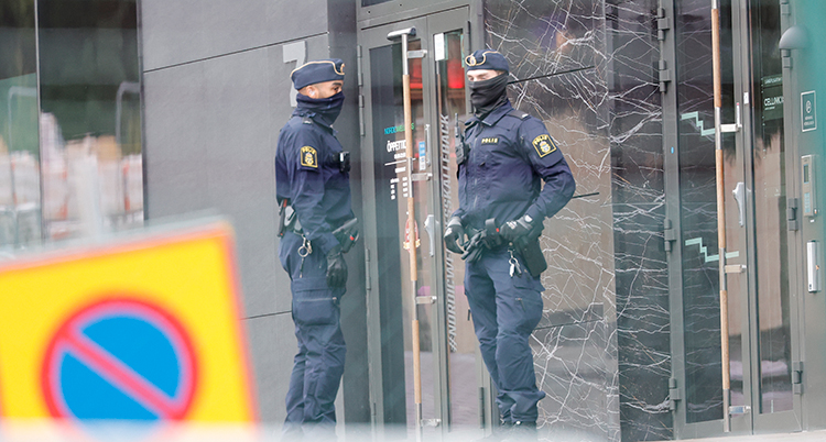 Två maskerade poliser står utanför en port.