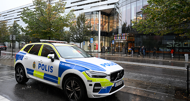 En polisbil står på vägen utanför ett stort hus i glas.