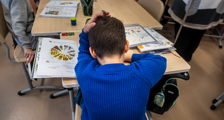 En kille i blå tröja sitter och jobbar med en uppgift i skolan.