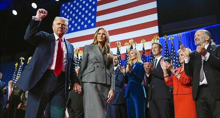 Donald Trump står på en scen. Han håller hand med sin fru. Han knyter den andra handen i luften. Folk står på scenen och applåderar.