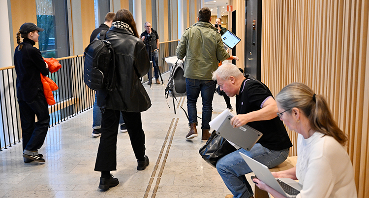 Flera personer med datorer står och sitter i en korridor i en domstol.