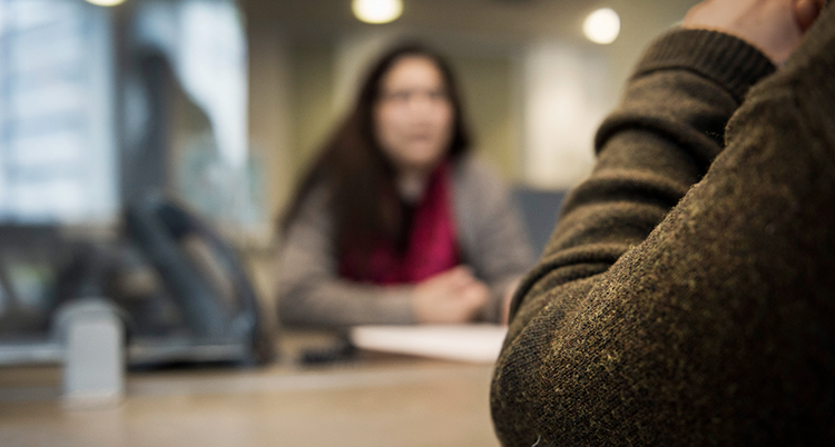 Två personer sitter och pratar vid ett bord på Migrationsverkets kontor.