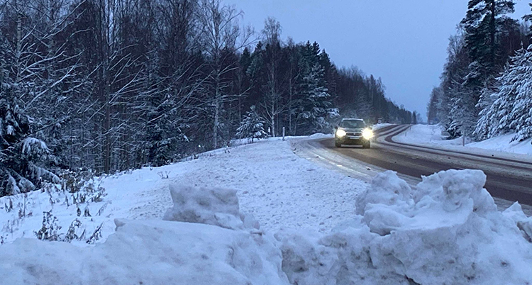 En bil kör på en väg. Det är mycket snö vid vägen.