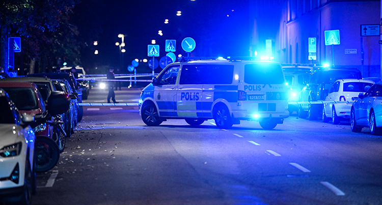 En gata i Stockholm. Det är mörkt ute. Poliserna har spärrat av. En polisbil med blåljus.