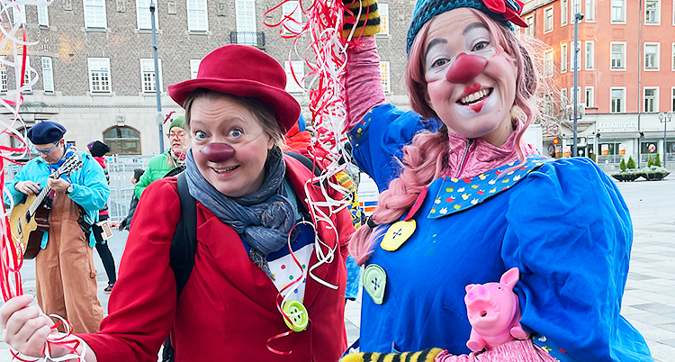 En clown har röd näsa, röd hatt och röd kavaj. Den andra har en blå klänning och en stor röd näsa.