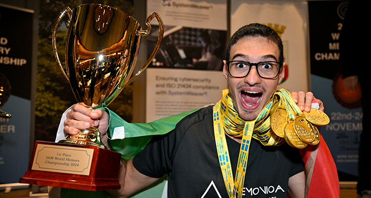 Han jublar in i kameran. Han har många guldmedaljer runt halsen och håller i en stor pokal.