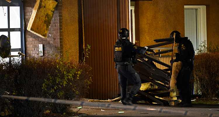 Två poliser med hjälmar jobbar utanför en skadad port. Det är mörkt.