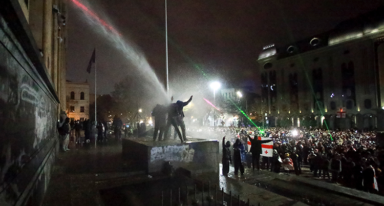 Människor på ett stort torg. Någon sprutar vatten på dem.